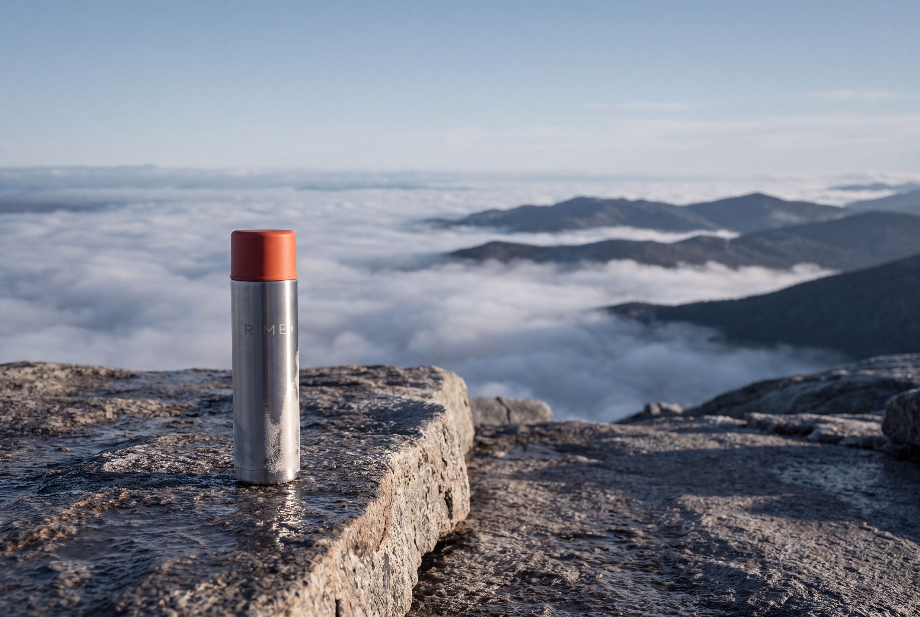 The flask on a rock ledge above a cloud inversion, lit by warm first light